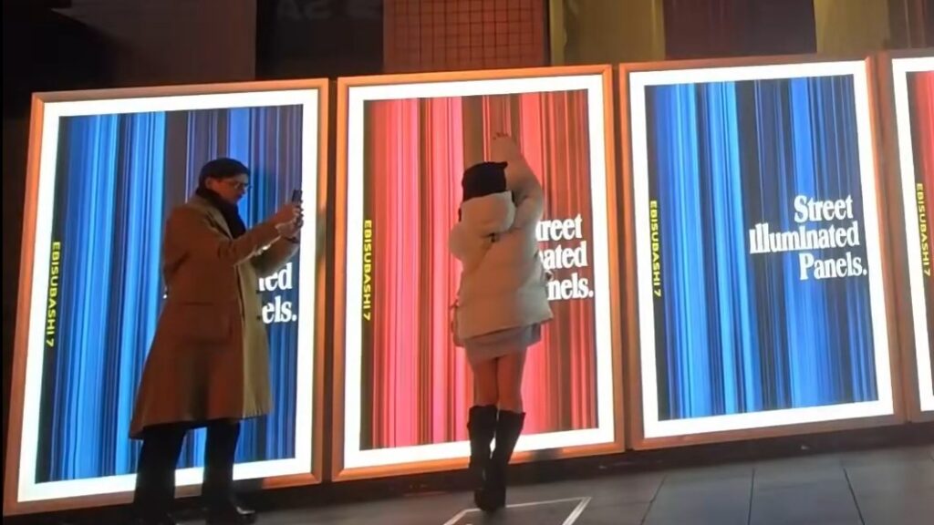 Hazu posing next to some signs for the lighting with Harry coaching her on the poses.